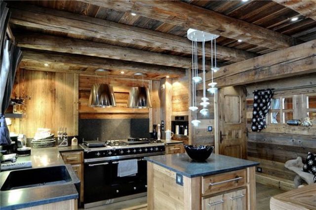 A light colored chalet kitchen with wooden beams, stone countertops, built in lights and pendant lamps