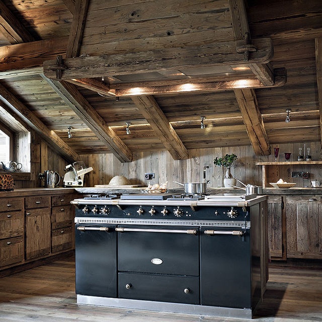 A rustic chalet kitchen all clad with reclaimed wood, with a large vintage kitchen island and built in lights looks welcoming and cozy