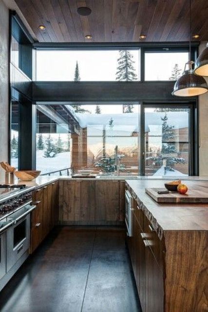 a contemporary chalet kitchen clad with reclaimed wood, with glazed walls, a wooden kitchen island and pendant lamps over it