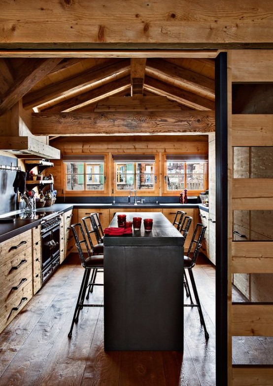 a cozy chalet kitchen decorated with reclaimed wood, with stone countertops, a stone kitchen island and a wooden screen or sliding door
