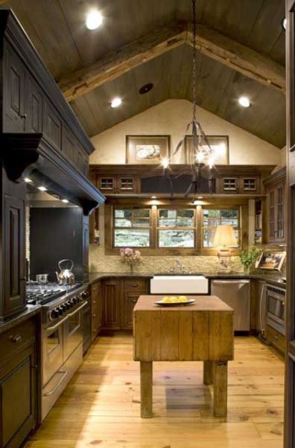 A cozy chalet kitchen with white stone walls, dark cabinets and a hood, a wooden kitchen island and built in lights