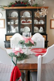 evergreens and red bows, a red stand, paper snowflakes and a Christmas arrangement with evergreens, berries and pinecones
