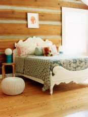 a cute rustic girl’s room clad with wooden planks, with a carved wooden bed and pastel bedding, poufs and a nightstand and a creative lamp