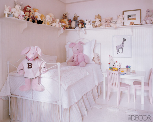 A neutral and light pink girl's room with a small metal bed with neutral bedding, a play dining set, an open long shelf with all the toys stored and displayed