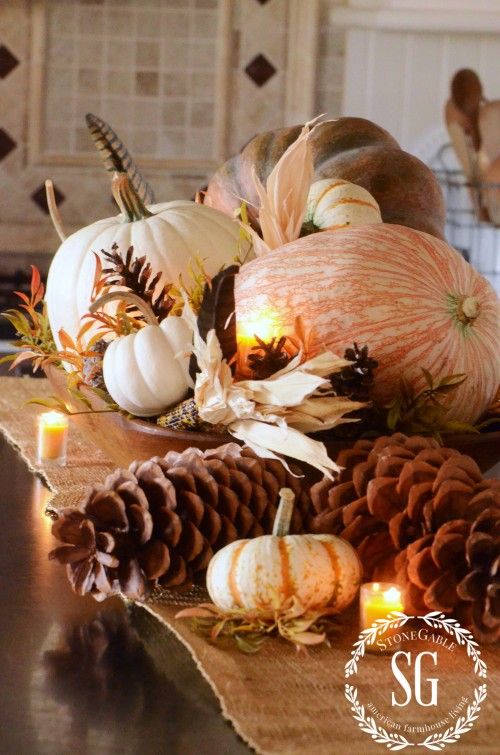 a lush fall centerpiece of oversized pinecones and pumpkins, fall leaves and corn husks plus candles is ideal for a Thanksgiving party
