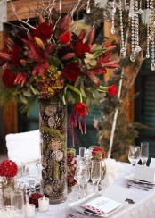 a refined Thanksgiving centerpiece of a tall vase filled with moss and pinecones and bold burgundy blooms and greenery