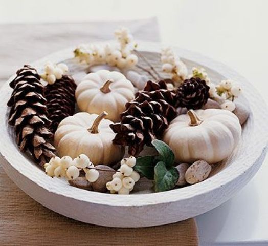 a chic neutral fall centerpiece of a white bowl filled with pinecones, white pumpkins, pebbles and white berries