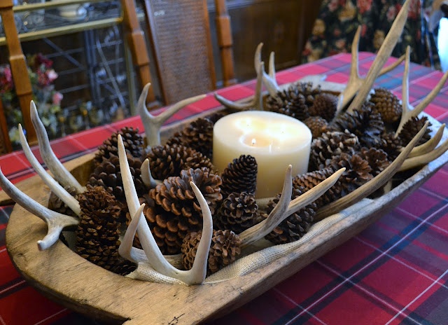 A rustic fall centerpiece of a dough bowl with pinecones, antlers and a large candle in the center