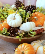 a stylish harvest-inspired centerpiece of a wooden bowl, foliage, corns and acorns,pinecones and various pumpkins