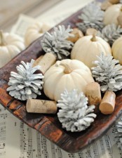 a quirky fall centerpiece of a wooden bowl, white pumpkins, whitewashed pinecones and wine corks