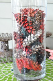 a simple fall centerpiece of a tall clear vase filled with dip dyed pinecones is veyr easy and fast to make