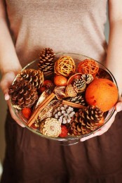 a glass bowl with pinecones, nuts, acorns, cinnamon sticks and colorful yarn balls