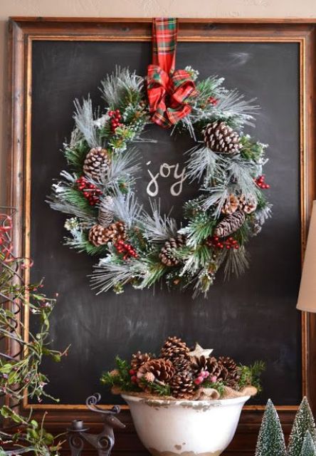 a flocked evergreen wreath with pinecones, berries, a red plaid bow is a pretty and cool decoration for indoor and outdoor decor