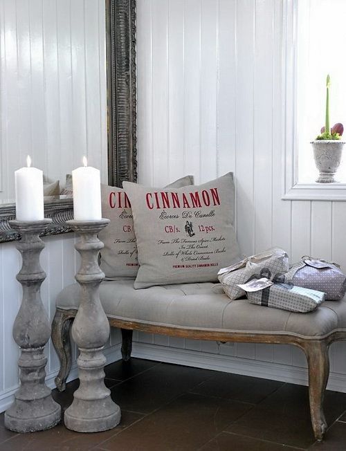 Grey pillows with red prints on them, a refined grey bench with gifts and tall wooden candleholders for sophisticated vintage inspired Christmas decor