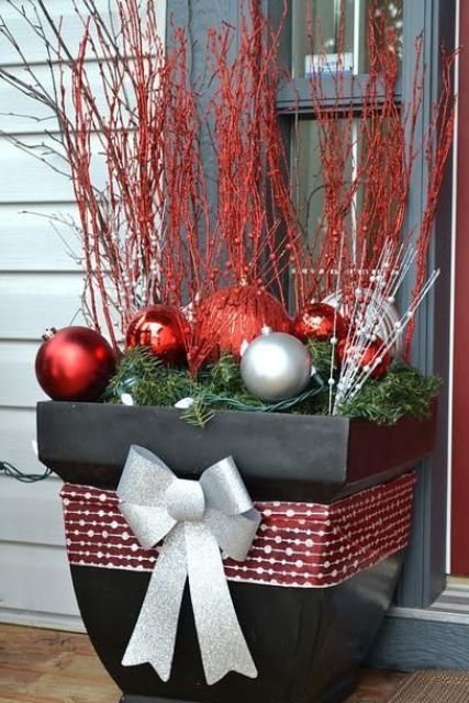 an oversized black planter with a silver grey and grey ribbon bow, silver and red ornaments and red branches is a bold and pretty decoration