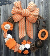 a rustic Halloween wreath of vine, with a printed orange bow, letters, fabric blooms and bows is bright and fun