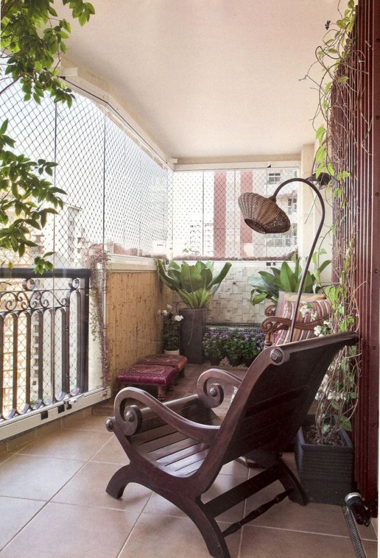 a rustic meets boho balcony with dark stained furniture, a wicker floor lamp and much greenery