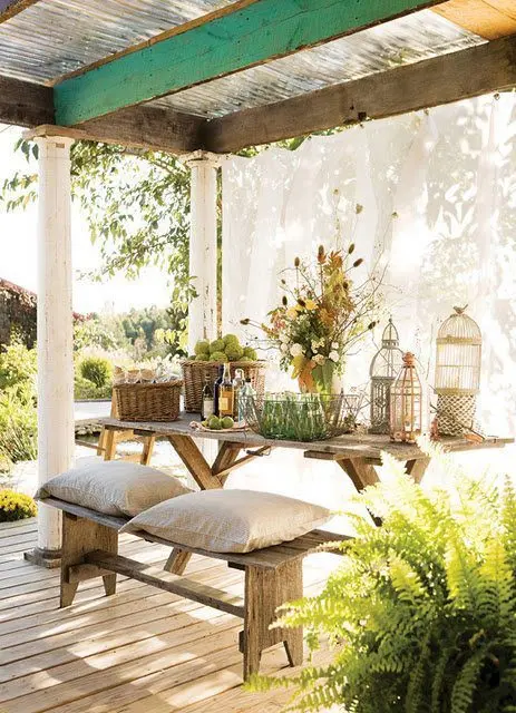 a welcoming rustic patio with pillars, curtains, wooden furniture and potted greenery