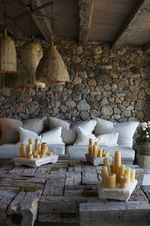 a rustic patio with stone walls, wicker lamps, a low rough wood table with lots of candles