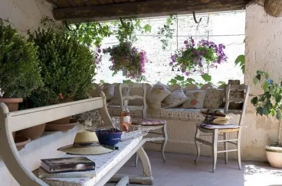 a neutral patio with stone walls, whitewashed wooden furniture, potted greenery and blooms