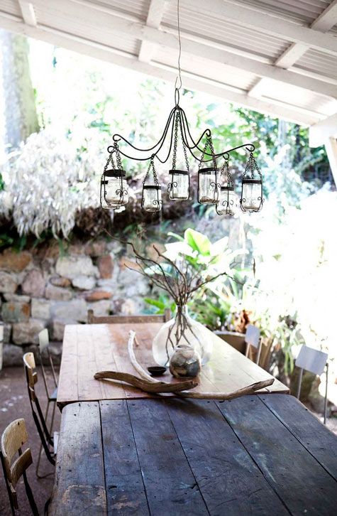 a rustic patio with stone walls, wooden furniture and candle lanterns hanging over the table
