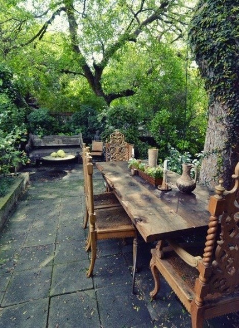 a rustic patio with a tile floor, a wooden bench and a wooden dining set plus much greenery
