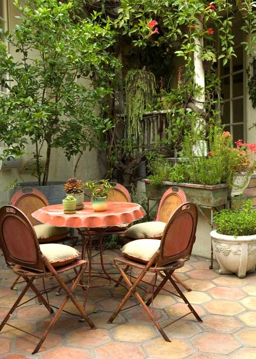 a rustic meets vintage patio with vintage wooden chairs and a table, potted greenery and blooms around