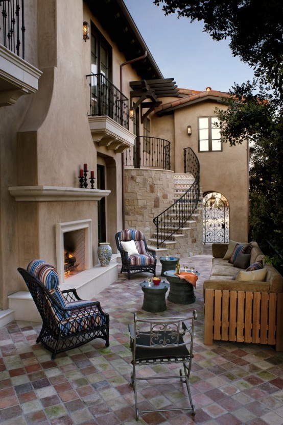 an elegant patio with a rustic feel, a neutral fireplace, wooden and wicker furniture and colorful textiles