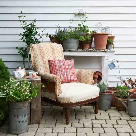 a cozy rustic nook with a vintage chair, bright pillows and potted blooms and greenery