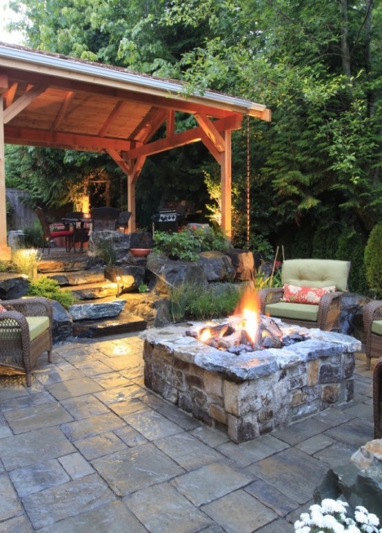 a rustic space done with tiles and stone, with a fire pit, comfy furniture and an outdoor kitchen