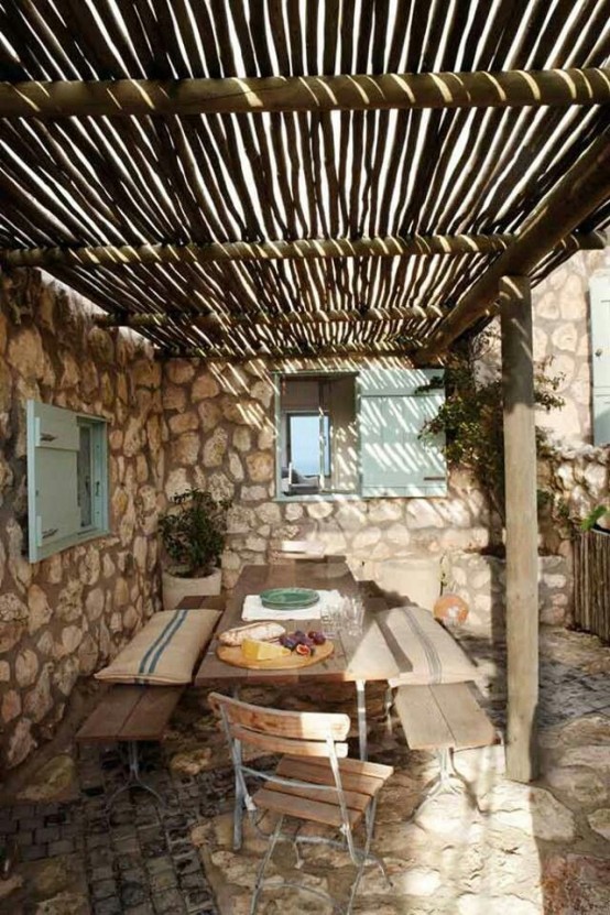 a rustic space with stone walls, wooden furniture, potted greenery and striped pillows