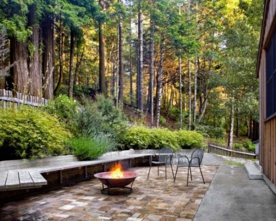 a contemporary meets rustic patio with a long wooden bench, a fire pit and a couple of chairs