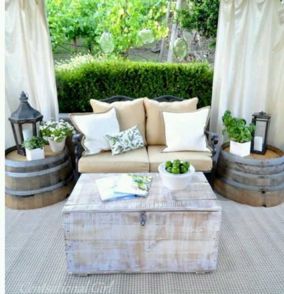 a bright rustic patio with barrels as side tables, a wooden chest, a comfy sofa and curtains for privacy