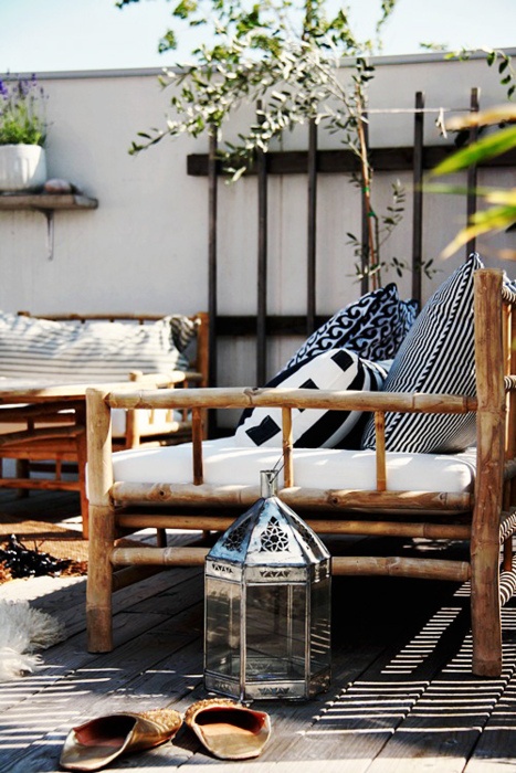 a cozy Scandinavian meets rustic patio with rattan furniture, black and white textiles and metal lanterns