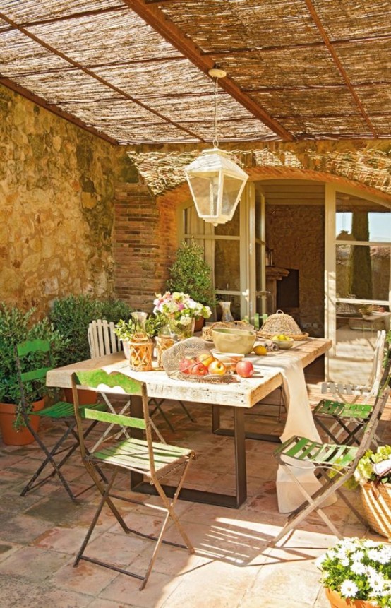 a French countryside patio with stone walls, wooden and metal furniture and a pendant lamp