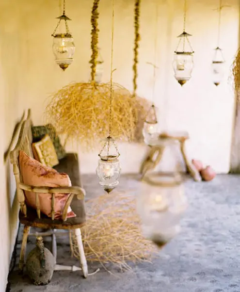 a vintage meets rustic patio with a wooden bench, some hay and pendant lamps