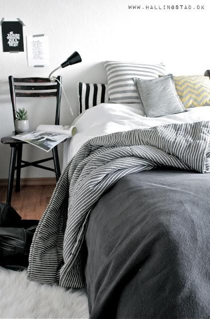 a chic Nordic bedroom with a black bed, striped bedding, a black chair, a catchy lamp