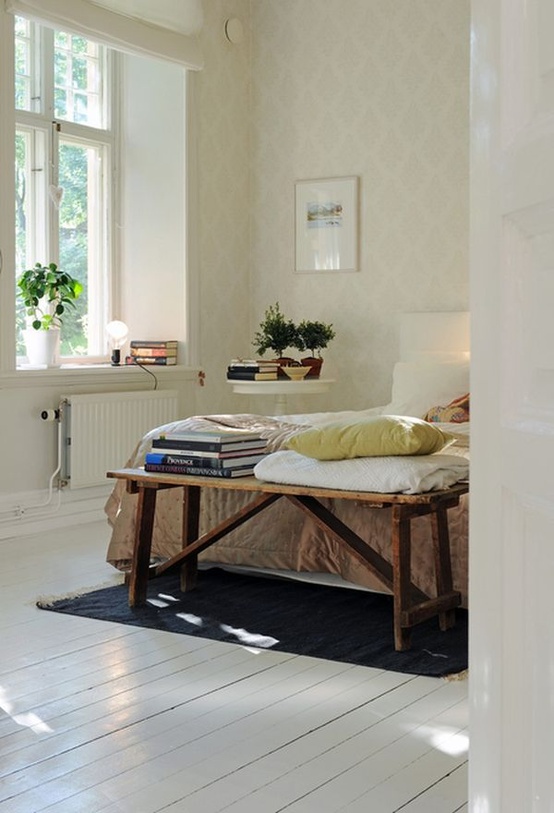 a cozy Scandi bedroom with printed wallpaper, a white wooden floor, a white bed and a rough wooden bench at the foot