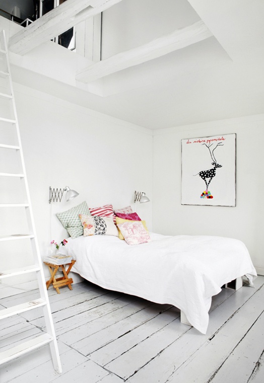 an airy Scandinavian bedroom with only a bed, a folding chair and an artwork plus whitewashed wooden floor