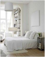 an airy Nordic bedroom with white furniture and bedding, an artwork, a pendant lamp and a crib hanging next to the bed