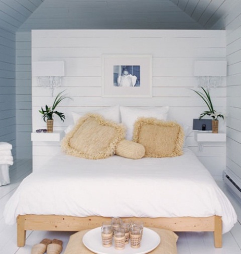a Noridc meets coastal bedroom done in white and blues, wiht a wooden bed and wicker touches plus potted greenery