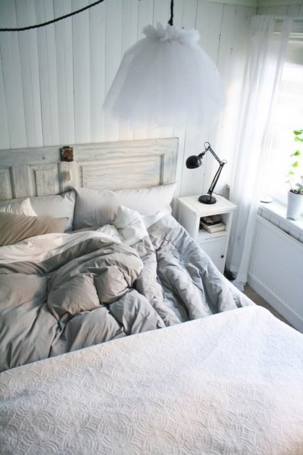 An air filled Scandinavian bedroom with white walls, a whitewashed wooden bed, white nightstands and pendant lamps