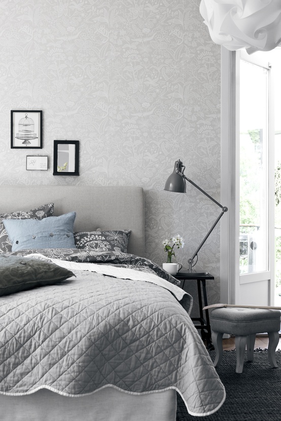 a Nordic bedroom done in grey, with printed wallpaper, an upholstered grey bed, printed bedding and a nightstand