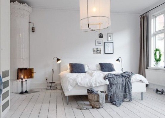 a peaceful white Scandinavian bedroom with a traditional stove, an upholstered bed, a pendant lamp