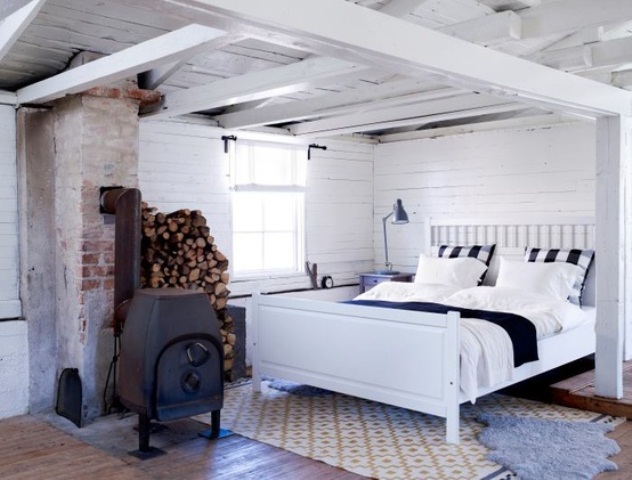 A vintage inspired Nordic bedroom in white, with white planks, a metal hearth and a comfy bed plus rugs