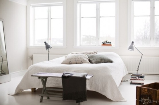 an airy and light-filled bedroom with a bed, a bench, some lamps and much natural light