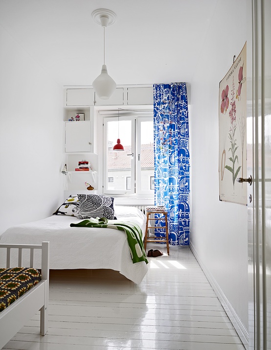 An airy minimal Scandinavian bedroom with a white bed, built in storage units and bright textiles