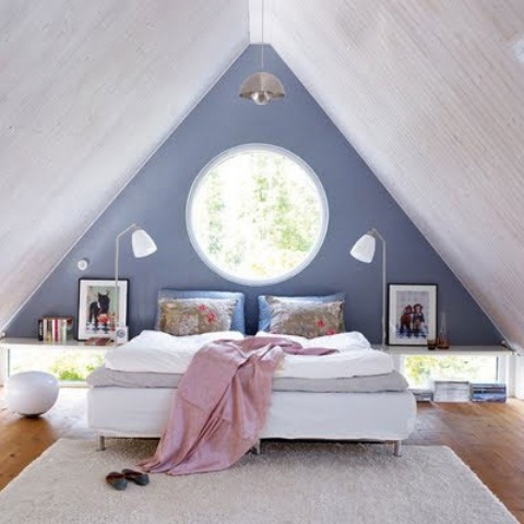 an attic bedroom with a blue and gray walls, wooden attic, a white bed, a carpet and some skylights and windows
