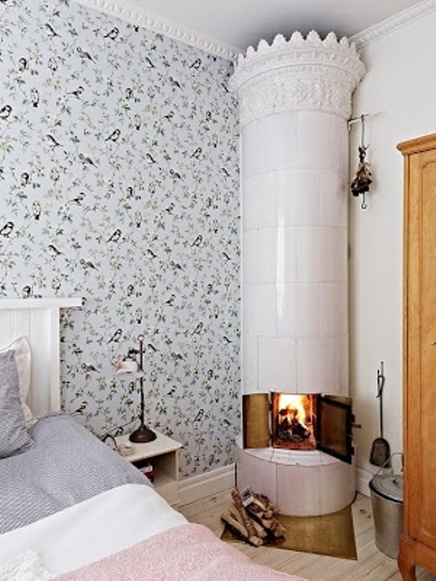 an airy Nordic bedroom with floral wallpaper, a white stove and pastel bedding