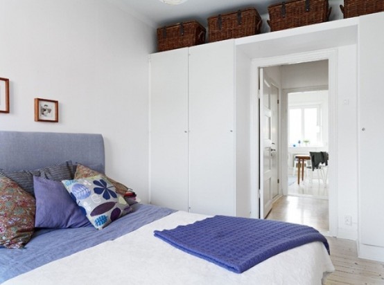 an airy Scandinavian bedroom in white, with purple touches, sleek storage units and baskets for storage